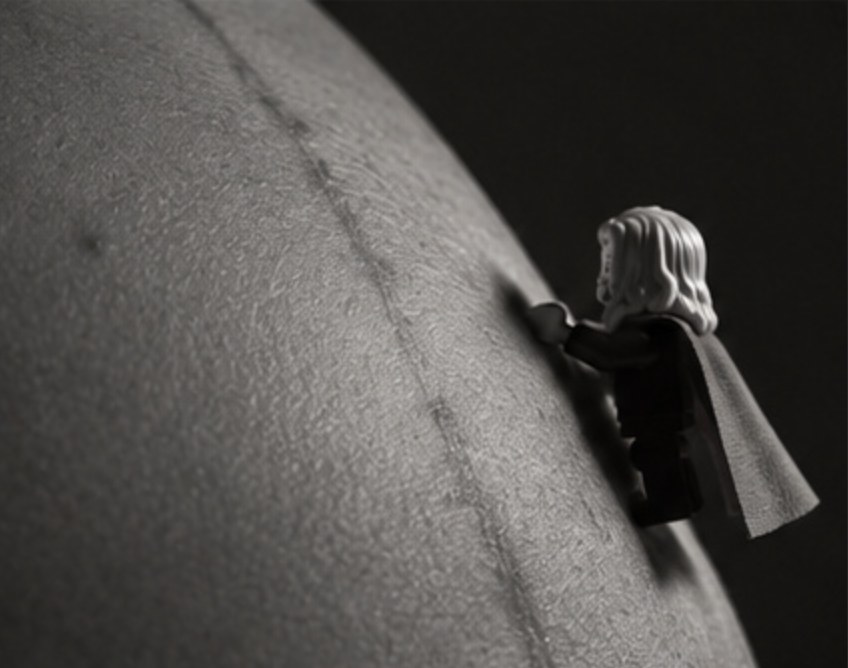 The figure climbs a belly following the dark vertical line of pregnancy