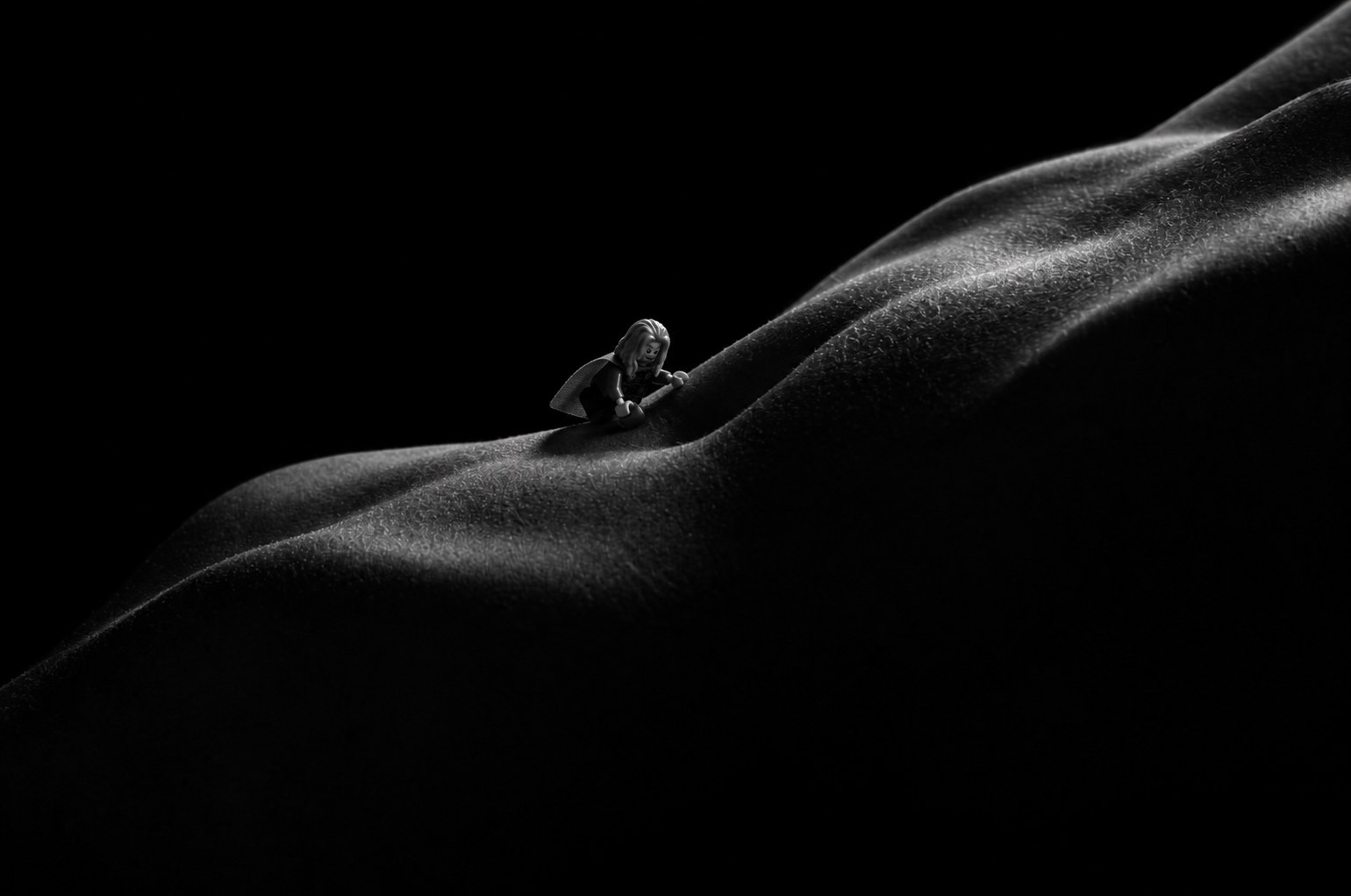 The figure climbs a slope of skin out of deep shadow